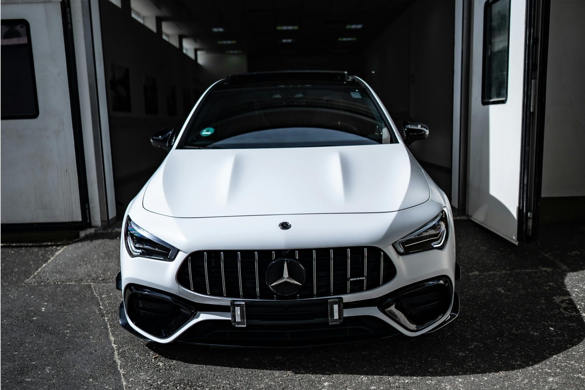 Front view of a sleek white Mercedes-Benz parked in a stylish garage entrance, showcasing luxury and elegance.